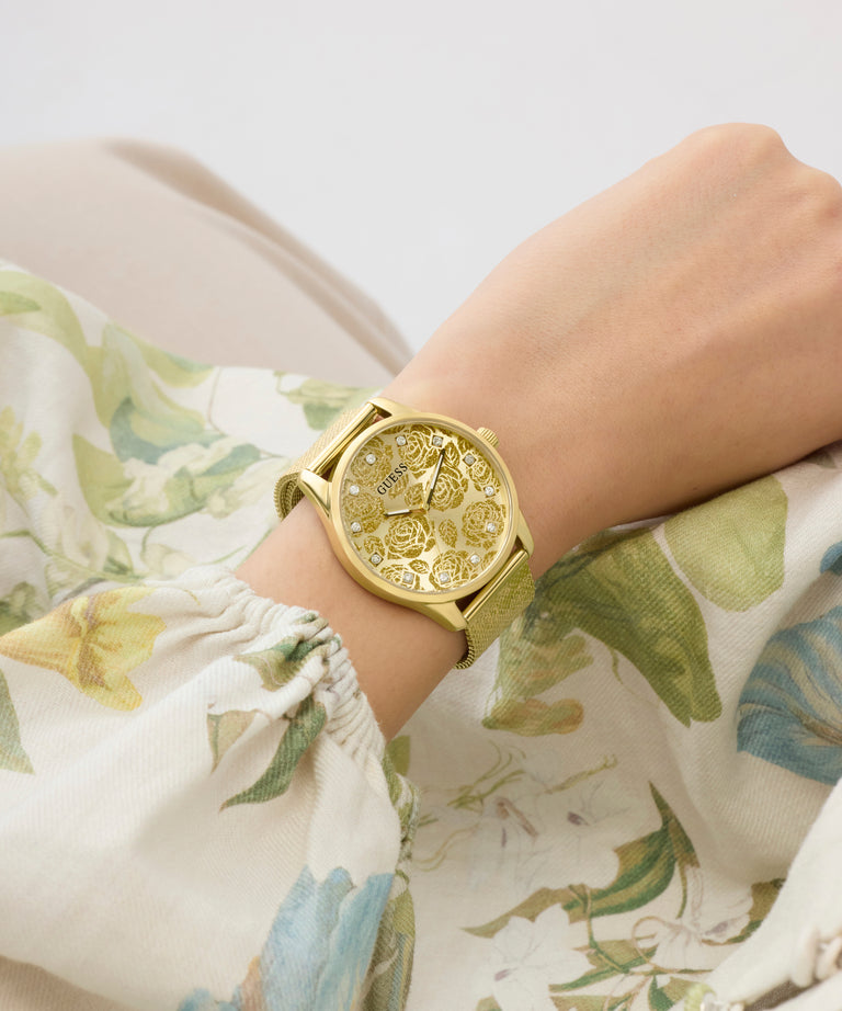 Gold GUESS Ladies Gold Tone Analog Watch on a wrist with floral-patterned fabric background