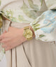 Gold GUESS Ladies Gold Tone Analog Watch on a wrist with a floral-patterned shirt and beige pants
