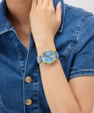 Person wearing a GUESS Ladies Blue Gold Tone Analog Watch with a blue face and gold casing on a denim jacket.