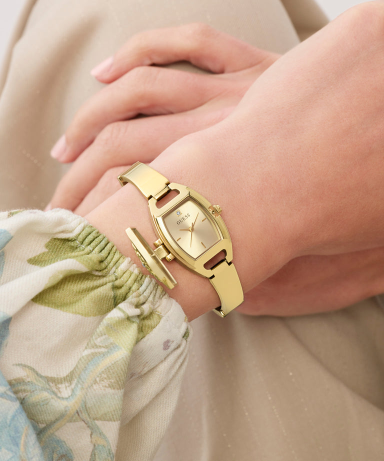 Gold GUESS Ladies Gold Tone Analog Watch on a wrist with a neutral background