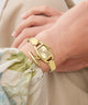 Gold GUESS Ladies Gold Tone Analog Watch on a wrist with a neutral background
