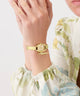 Gold GUESS Ladies Gold Tone Analog Watch on a wrist with a floral-patterned sleeve against a light background