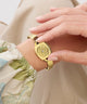 Gold GUESS Ladies Gold Tone Analog Watch with a decorative clasp worn by a person against a neutral background