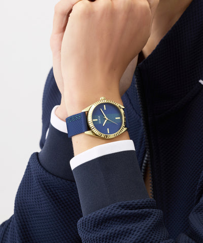 Hand wearing a Guess watch with a blue strap on a neutral background