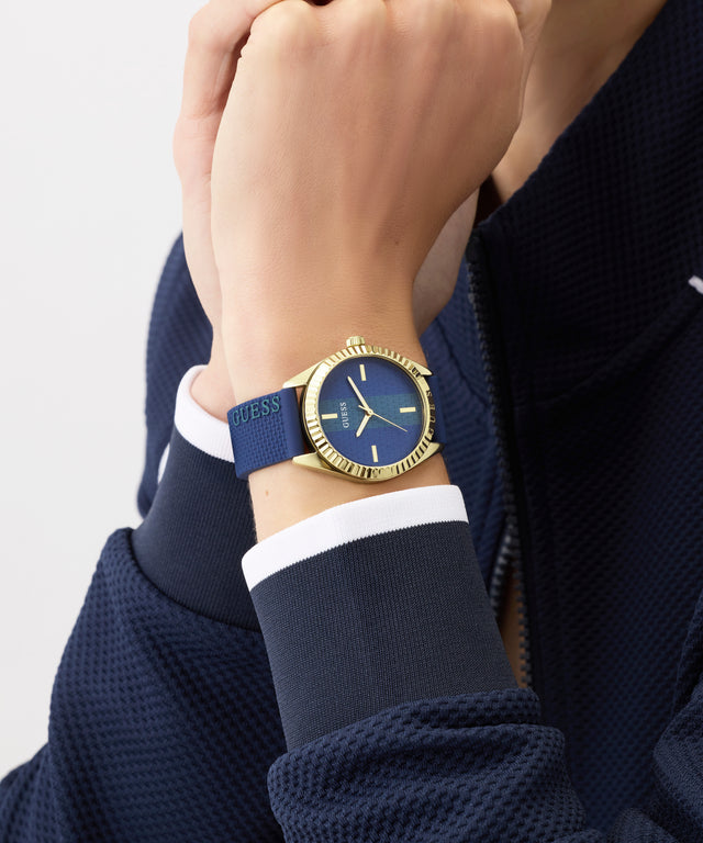 Hand wearing a Guess watch with a blue strap on a neutral background