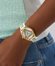 Wrist wearing a colorful GUESS Ladies Pride Limited Edition White Gold Tone Analog Watch with a rainbow band against a neutral background