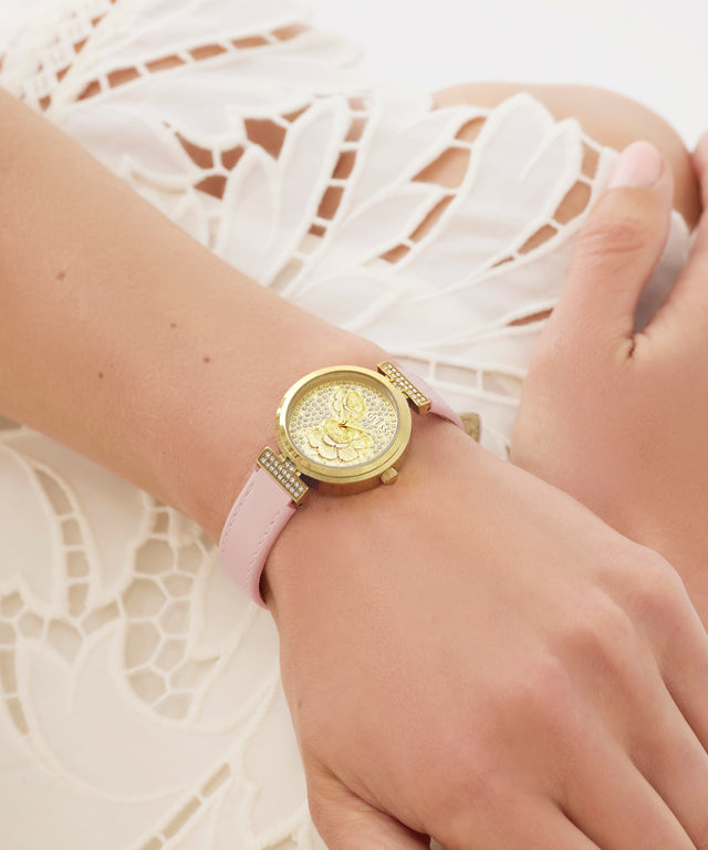 GUESS Ladies Light Pink Gold Tone Analog Watch watch with a pink strap on a wrist against a white lace background