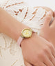 GUESS Ladies Light Pink Gold Tone Analog Watch watch with a pink strap on a wrist against a white lace background