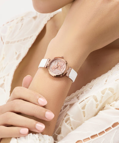 GUESS Ladies White Rose Gold Tone Analog Watch with white strap on a wrist against a white lace background