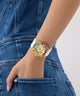 Gold GUESS Ladies Pride Limited Edition White Gold Tone Analog Watch with a white strap on a person's wrist, wearing blue jeans.