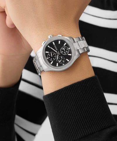 Silver GUESS Mens Palmer Silver Tone Analog Watch on a wrist with a black and white striped background