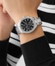 Silver GUESS Mens Palmer Silver Tone Analog Watch on a wrist with a black and white striped background