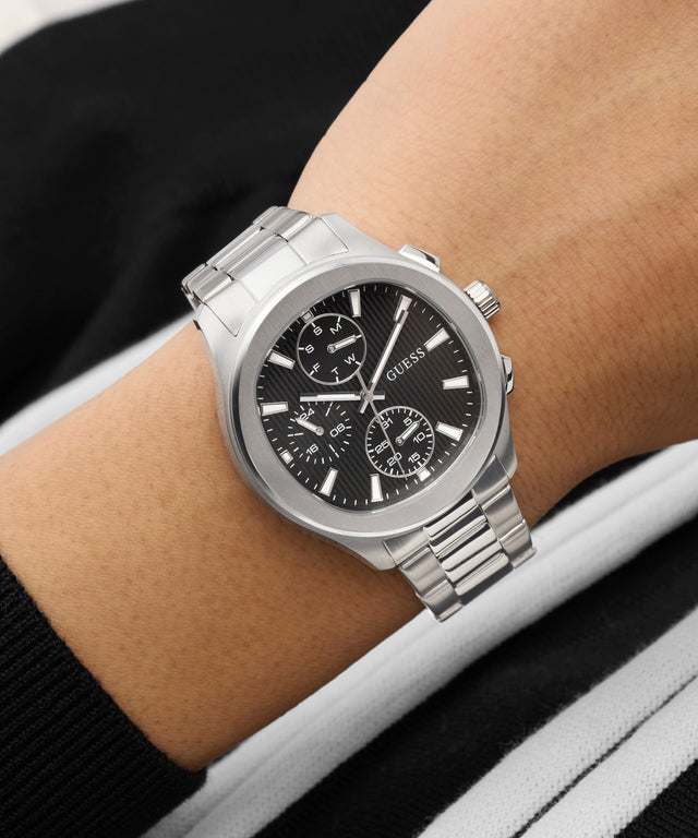Silver GUESS Mens Palmer Silver Tone Analog Watch with a black face on a wrist against a neutral background