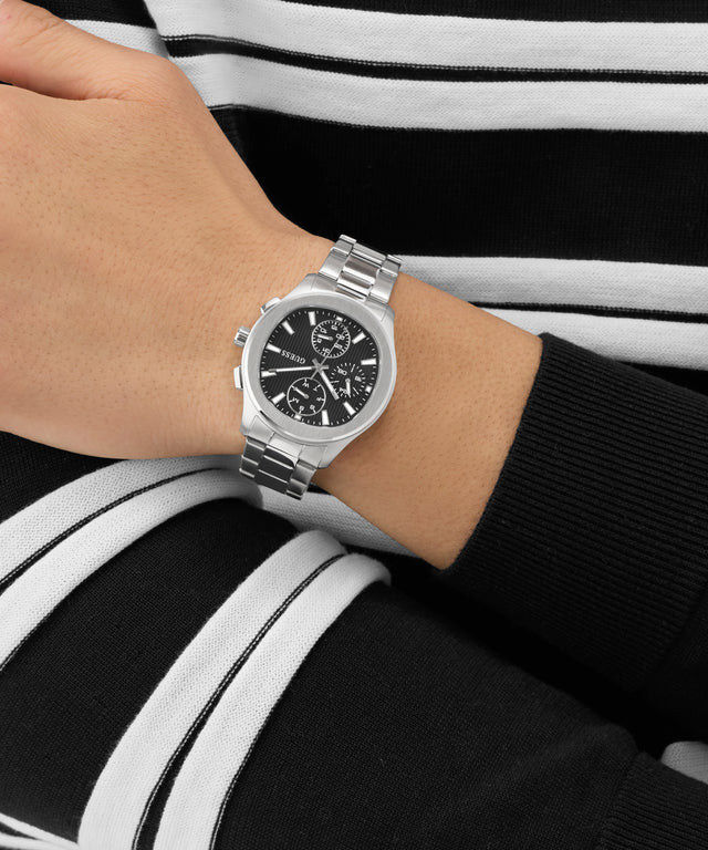 Silver GUESS Mens Palmer Silver Tone Analog Watch on a wrist with a black and white striped background