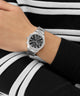 Silver GUESS Mens Palmer Silver Tone Analog Watch on a wrist with a black and white striped background