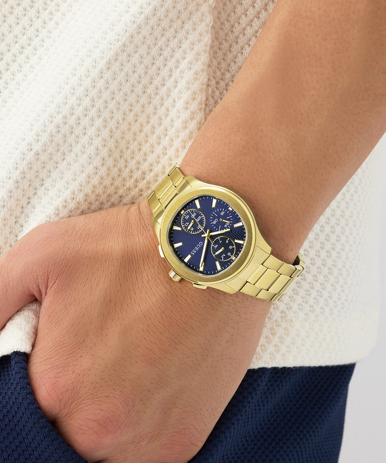 Gold GUESS Mens Palmer Gold Tone Analog Watch with a blue face on a wrist against a neutral background