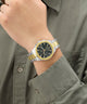 Gold and silver watch on a wrist with a green shirt