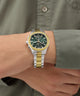 Two-tone GUESS Mens Palmer 2-Tone Analog Watch on a wrist with a green shirt background