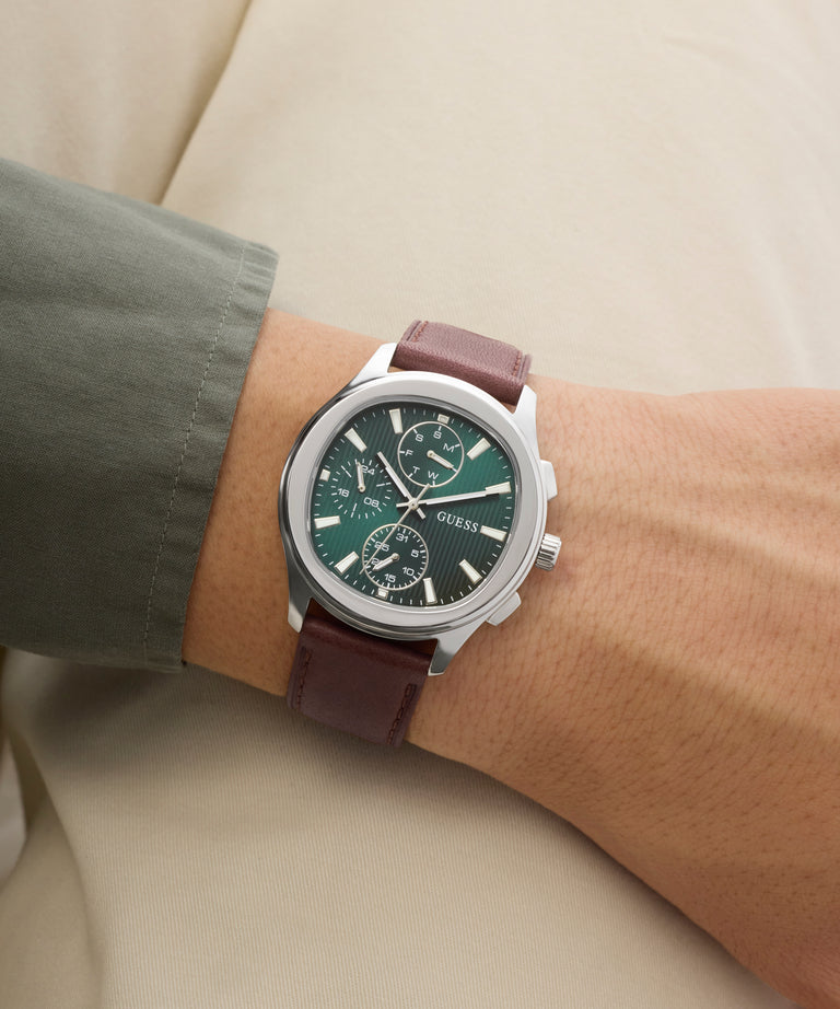 Wrist wearing a Guess watch with a brown leather strap and green dial.