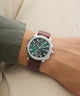 Wrist wearing a Guess watch with a brown leather strap and green dial.