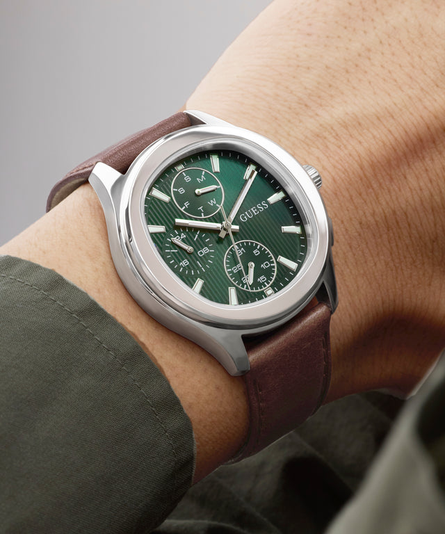 Wrist wearing a Guess watch with a green face and brown strap.