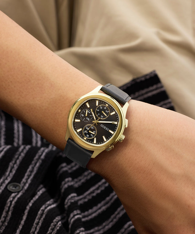 Gold watch with black strap on a wrist, wearing a striped shirt.
