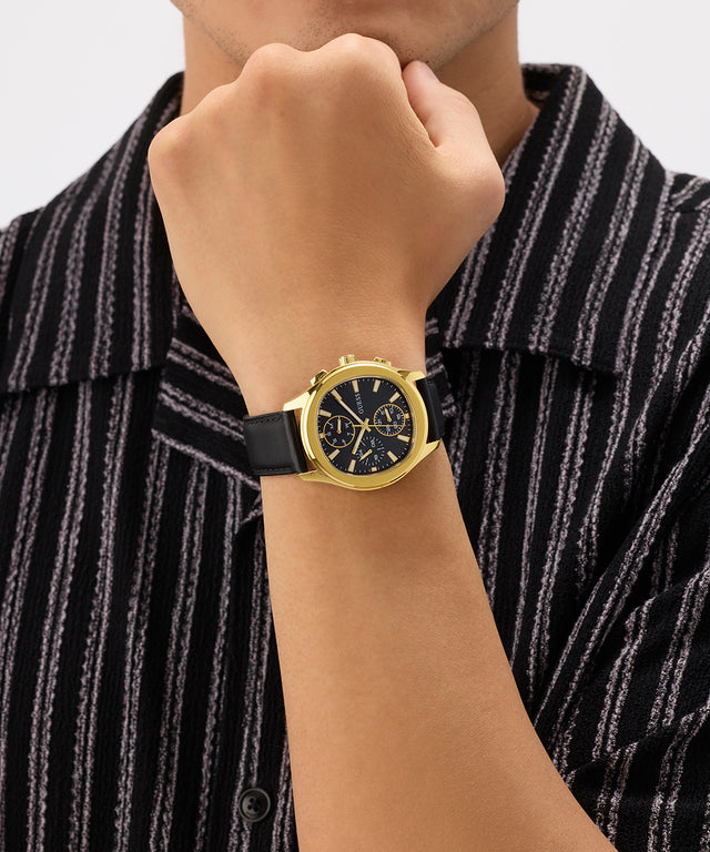 Gold watch on a wrist with a black strap against a striped shirt background