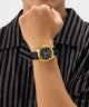 Gold watch on a wrist with a black strap against a striped shirt background