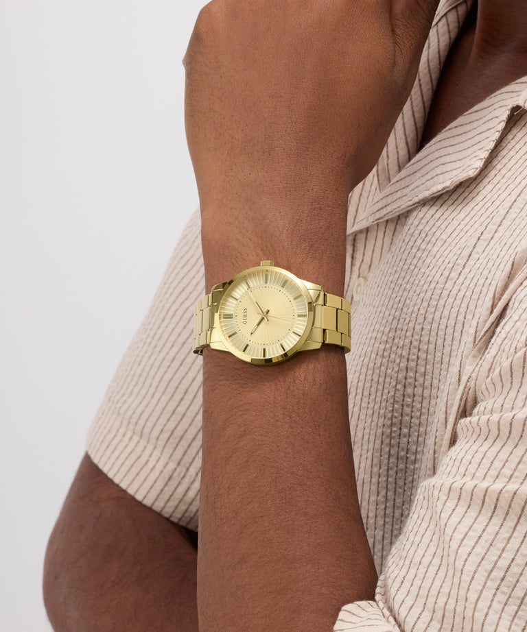 Gold GUESS Mens Gold Tone Analog Watch on a person's wrist with a neutral background