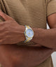 Gold watch on a wrist with a brown textured shirt