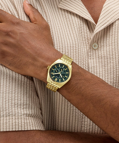 Gold GUESS Mens Gold Tone Analog Watch on a wrist with a neutral background