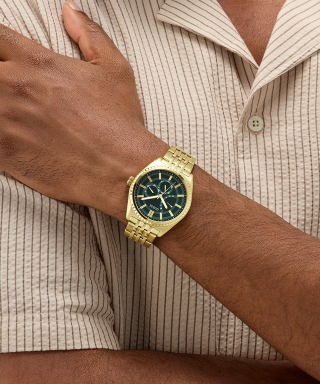 Gold GUESS Mens Gold Tone Analog Watch on a wrist with a neutral background