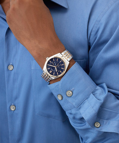 Person wearing a silver GUESS Mens 2-Tone Analog Watch with a blue face on a blue shirt.