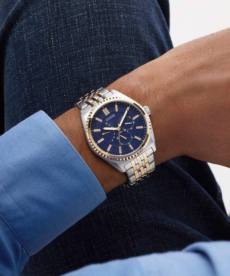 Gold and silver GUESS Mens 2-Tone Analog Watch with blue face on a wrist, wearing a blue shirt.