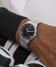 Person wearing a silver watch with a black face on a white background
