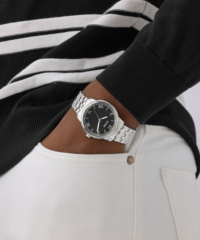 Person wearing a black and white striped sweater with a silver watch on a plain background
