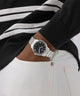 Person wearing a black and white striped sweater with a silver watch on a plain background
