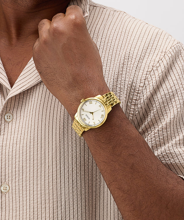 Gold GUESS Mens Gold Tone Analog Watch on a person's wrist with a neutral background