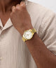 Gold GUESS Mens Gold Tone Analog Watch on a person's wrist with a neutral background