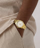Gold watch on a wrist with a neutral background