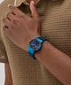 Person wearing a blue watch on a brown textured shirt