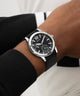 Close-up of a person wearing a GUESS Mens Black Silver Tone Analog Watch watch on a white background