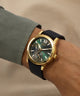 Gold watch with a black strap on a wrist against a beige background