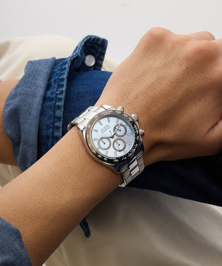 Person wearing a silver GUESS Mens Arthur Silver Tone Analog Watch with a white face on a neutral background