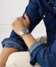 Person wearing a blue denim jacket with a GUESS Mens Arthur Silver Tone Analog Watch on a white background