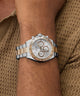 Silver and gold GUESS Mens Arthur 2-Tone Analog Watch on a wrist with a textured brown background