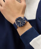 Blue GUESS Mens Midnight Blue Rose Gold Tone Analog Watch on a person's wrist with a dark blue and white jacket