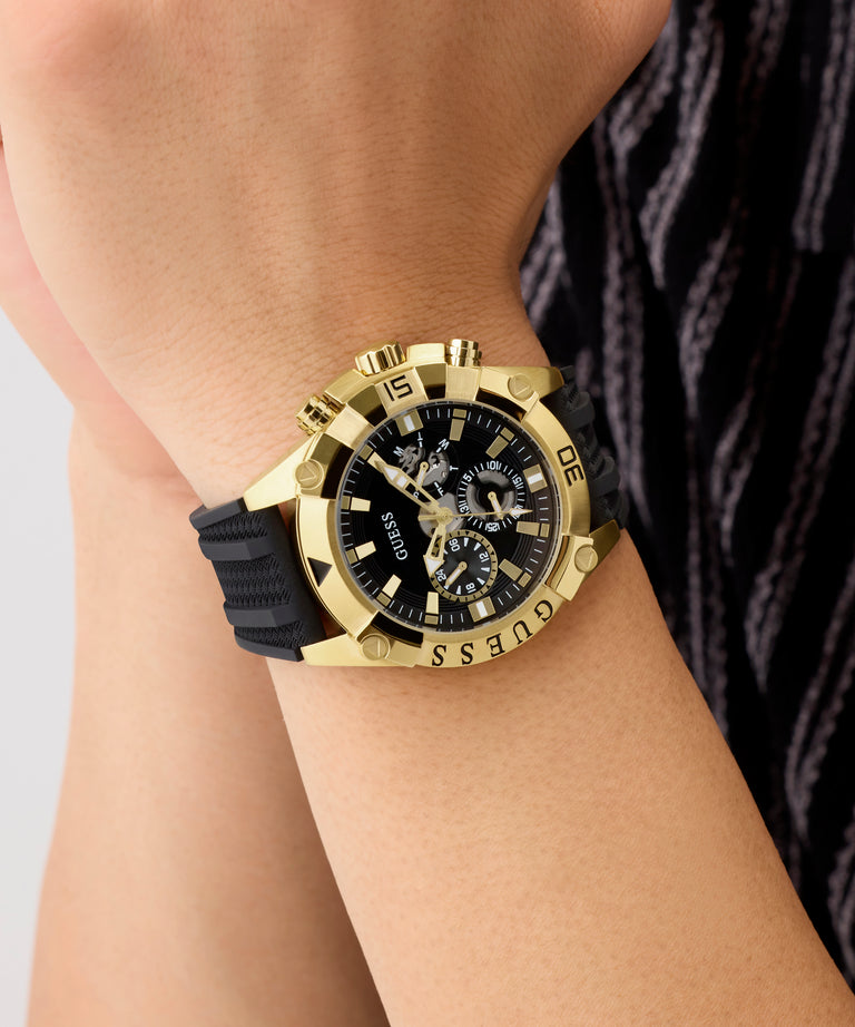 Gold and black Guess watch on a wrist with a neutral background