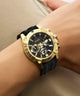 Gold watch with black strap on a wrist against a neutral background