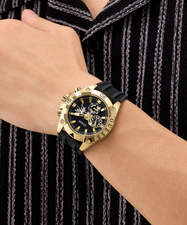 Gold wristwatch with black strap on a person's wrist against a black and gray striped background